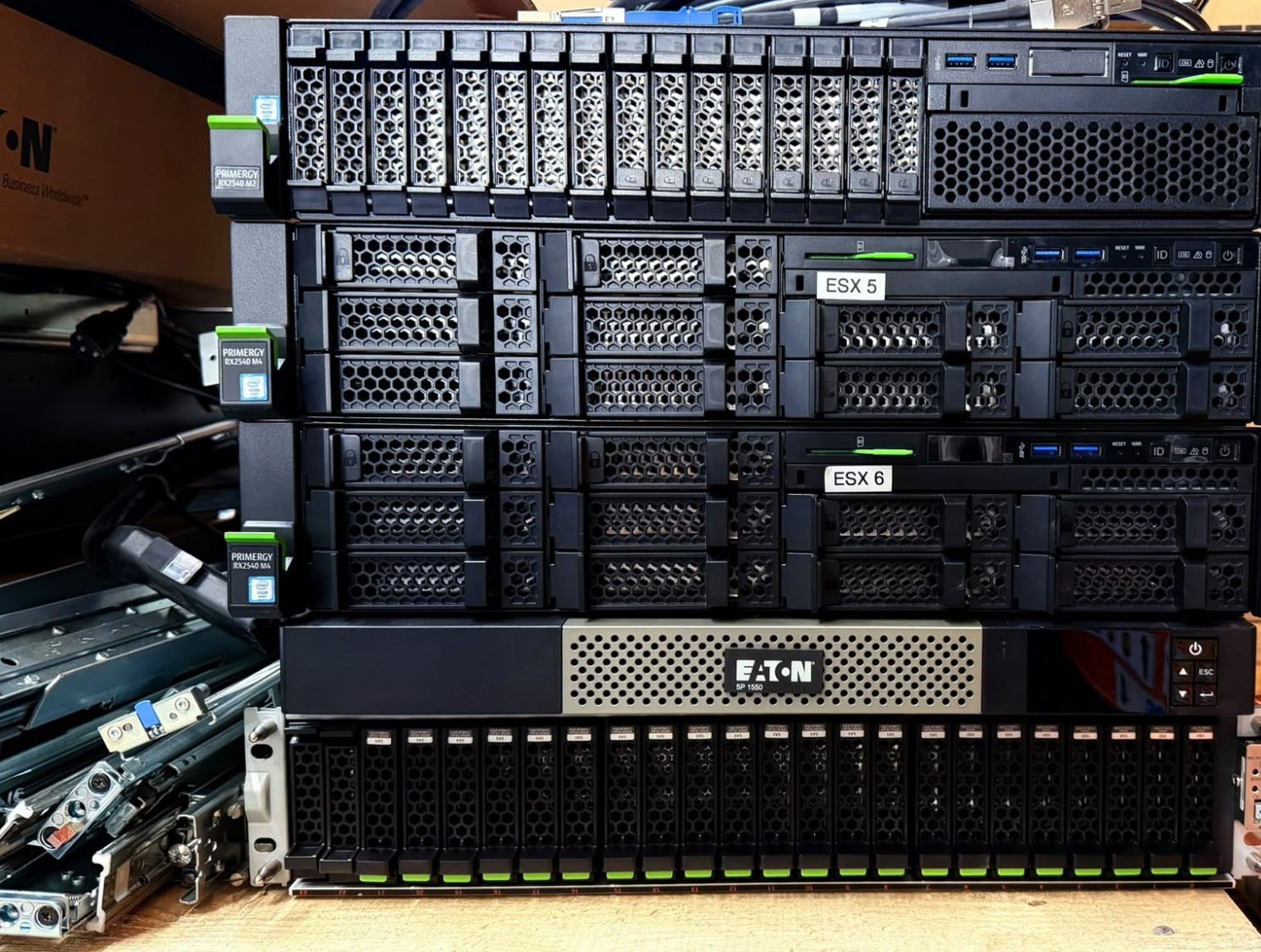 Trois serveurs Fujitsu PRIMERGY empilés, étiquetés ESX 5 et ESX 6, un onduleur Eaton et une baie de disques, posés sur un établi.