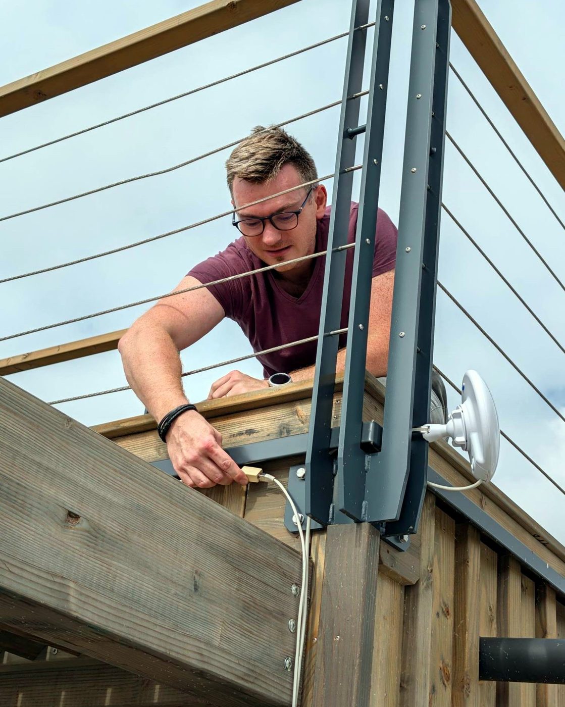 Un technicien raccorde une borne Wi-Fi extérieure fixée sur une structure en bois.
